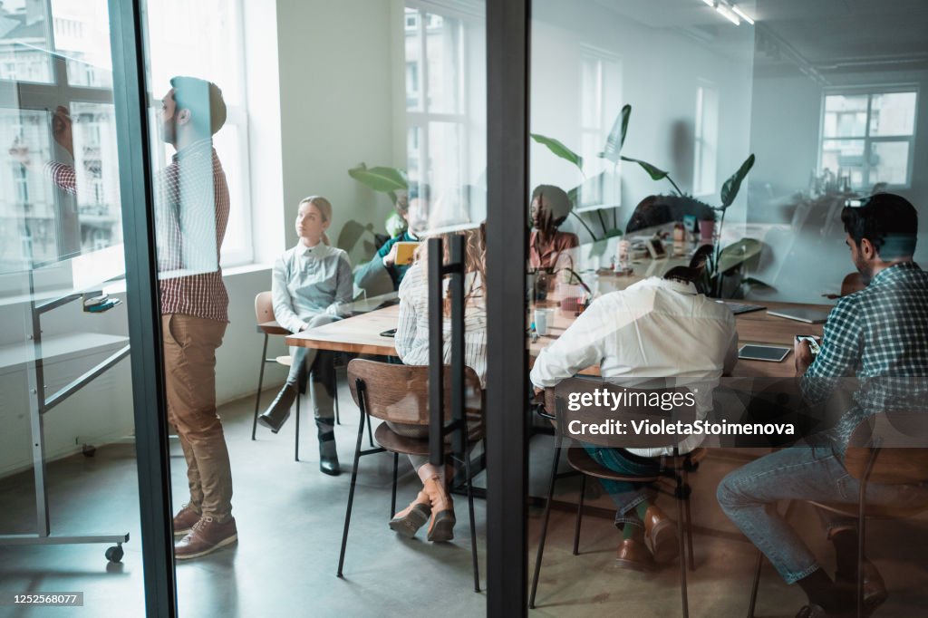 Jonge ondernemer die zijn medewerkers nieuwe bedrijfsstrategie op een vergadering presenteert.