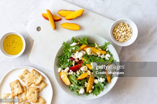 autumn salad of iceberg lettuce, spinach, peach and goat cheese in a white rustic plate on marble background with copy space - feta cheese imagens e fotografias de stock