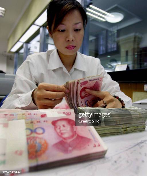 Bank teller counts the stack of Chinese yuan and US dollars at a bank in Shanghai, 22 July 2005. China's cautious revaluation of its yuan is set to...