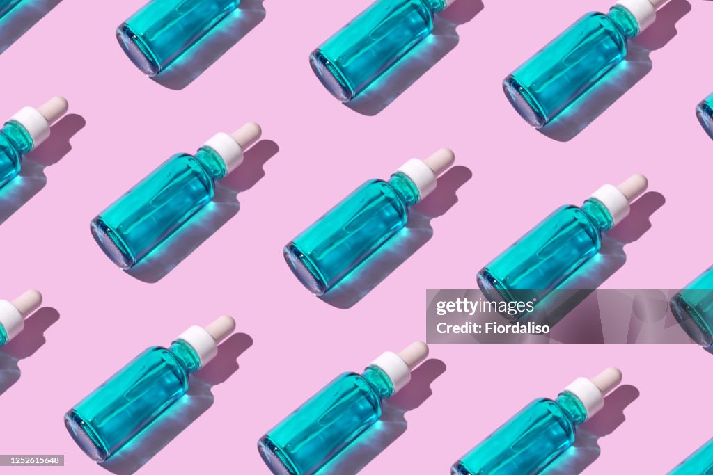 Transparent liquid dropper 
and blue bottle on pink pastel background