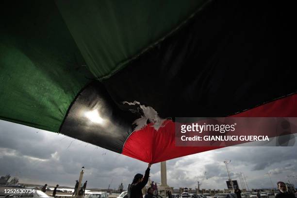 Libyan man holds a huge old national flag as thousands take part in an anti-regime rally through the streets of the eastern city of Benghazi on March...