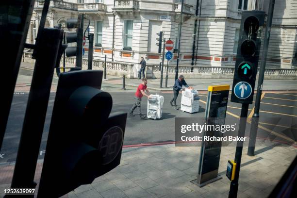Two men push copying equipment across a road, a delivery for a nearby business in Victoria, on 3rd May 2023, in London, England.