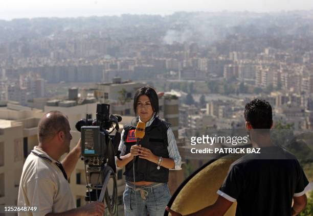 Journalist from LBCI television Mona Saliba reports in front of the camera in Beirut 24 July 2006 with smoke billowing in the background caused by...