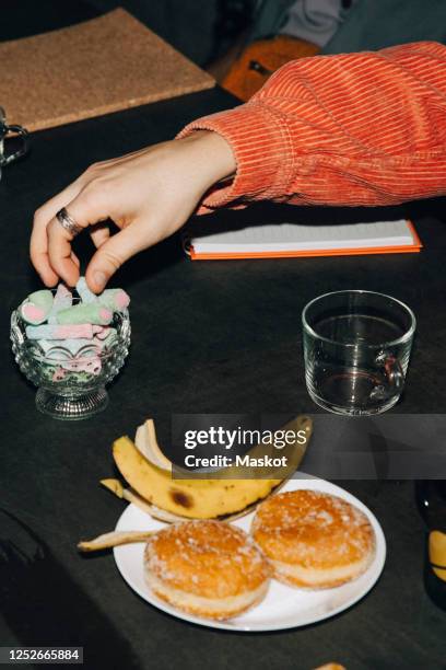 cropped hand of man eating candy at table in office - donut man bildbanksfoton och bilder