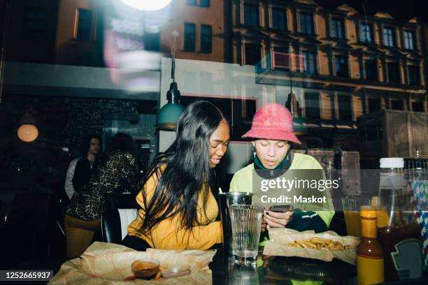 man showing smart phone to smiling woman seen through transparent glass window - snack table stock pictures, royalty-free photos & images