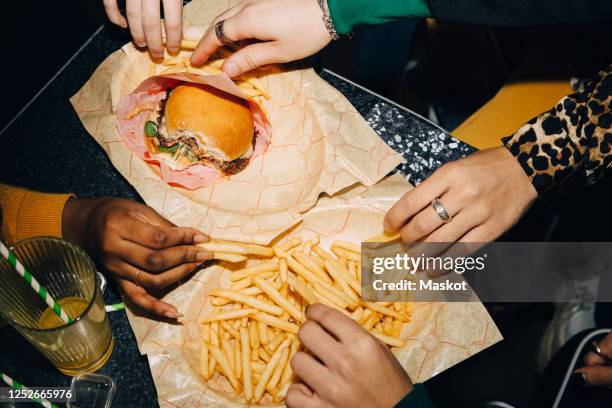 high angle view of friends eating burger and french fries at table in cafe - unhealthy eating ストックフォトと画像