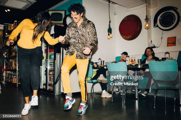 smiling young man and woman dancing while friends watching in background in cafe - patrón de leopardo fotografías e imágenes de stock