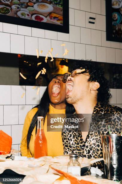 male and female friends with open mouth eating french fries in cafe - young adult male stock-fotos und bilder