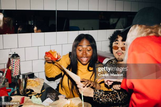 waitress pointing while woman with burger ordering food by friend in cafe - burger portrait stock-fotos und bilder