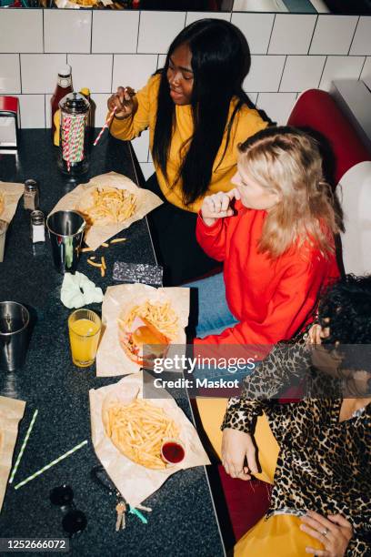 high angle view of male and female friends eating food at table in cafe - male burger eating fotografías e imágenes de stock