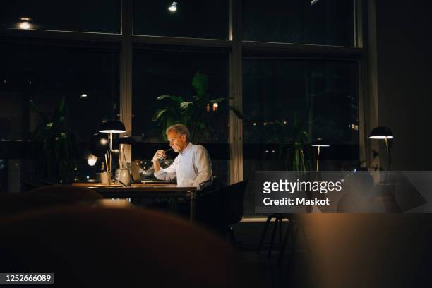 thoughtful businessman working late while sitting with laptop in dark workplace - working overtime stock pictures, royalty-free photos & images