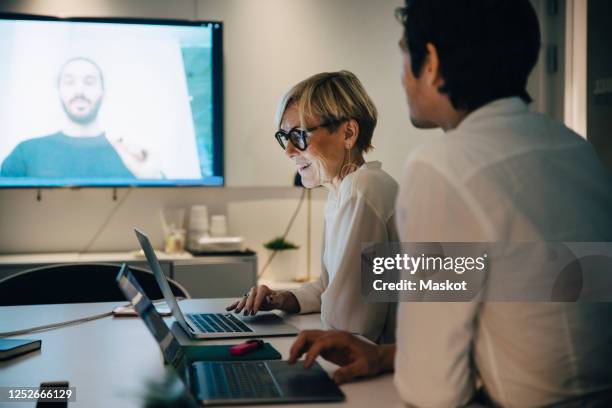 smiling businesswoman sitting with businessman in board room during video conference - meeting room screen stock-fotos und bilder