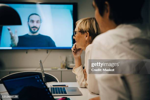 colleagues listening to businessman during video conference in board room at office - meeting room screen stock-fotos und bilder