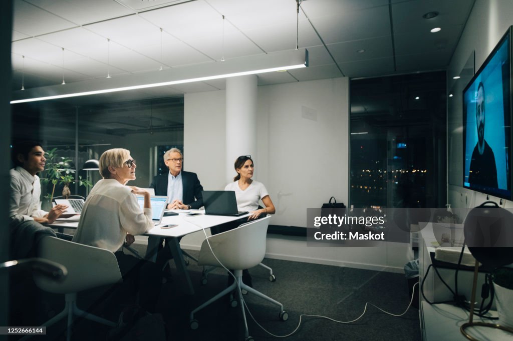 Colleagues looking at businessman during video conference meeting at night in office