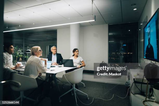 colleagues looking at businessman during video conference meeting at night in office - conference room screens stock pictures, royalty-free photos & images