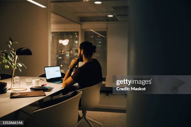 side view of dedicated male professional working late at illuminated desk in coworking space - männerabend stock-fotos und bilder