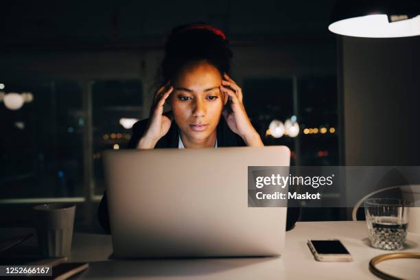 young female entrepreneur with headache while working late in office - überarbeitung stress stock-fotos und bilder