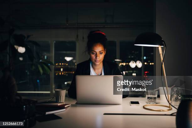 dedicated young businesswoman working late while using laptop at creative office - frau schreibtisch laptop büro stock-fotos und bilder