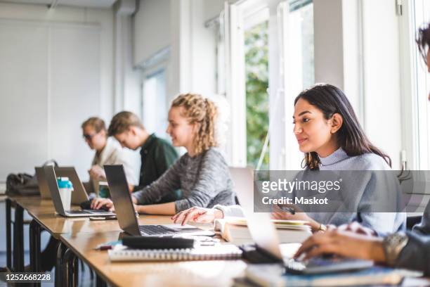 male and female students using laptops in classroom - universiteit stockfoto's en -beelden