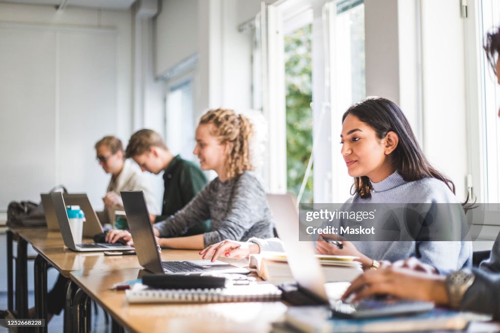 Male and female students using laptops in classroom