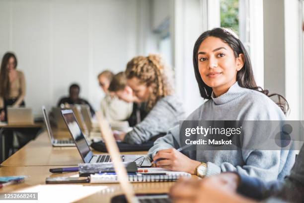 portrait of confident young woman at desk in classroom - indian college students imagens e fotografias de stock