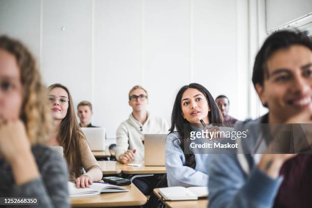 multi-ethnic male and female students sitting at desk in classroom - universiteit stockfoto's en -beelden