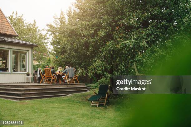 senior men and women enjoying dinner while sitting dining table during garden party - garden decking stock-fotos und bilder