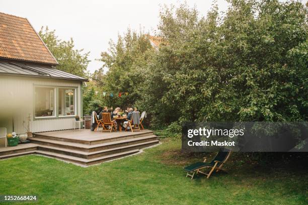 senior male and female friends enjoying dinner while sitting dining table during garden party - backyard stock pictures, royalty-free photos & images