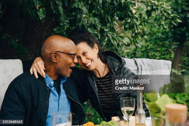 cheerful senior man and woman enjoying while sitting at dinning table during garden party - garden of laughs stockfoto's en -beelden