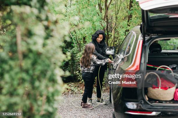 mid adult woman teaching daughter to charge electric car at charging station - hybrid car stock pictures, royalty-free photos & images