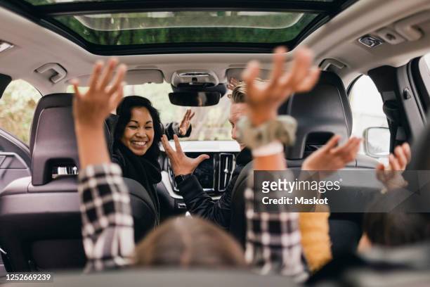cheerful family raising hands while enjoying road trip in electric car - auto familie stock-fotos und bilder