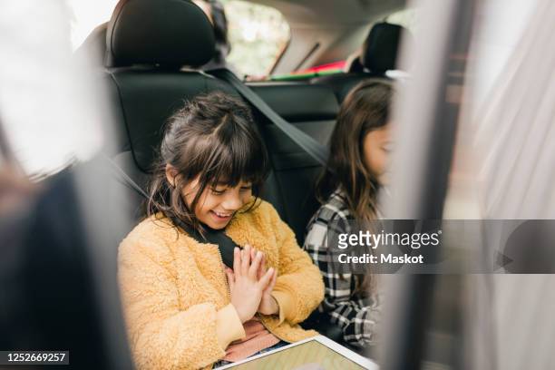 smiling girl using digital tablet while sitting in car - auto tablet stockfoto's en -beelden