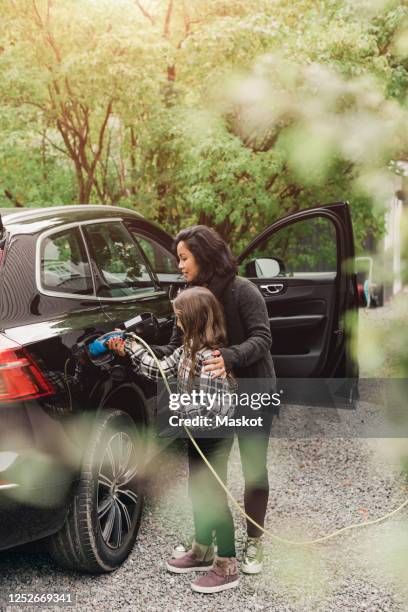 mid adult woman teaching daughter to charge electric car at charging station - daughter car stock pictures, royalty-free photos & images