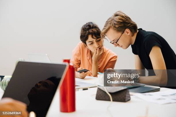 colleagues sharing smart phones while sitting in illuminated board room during meeting - androgyn foto e immagini stock