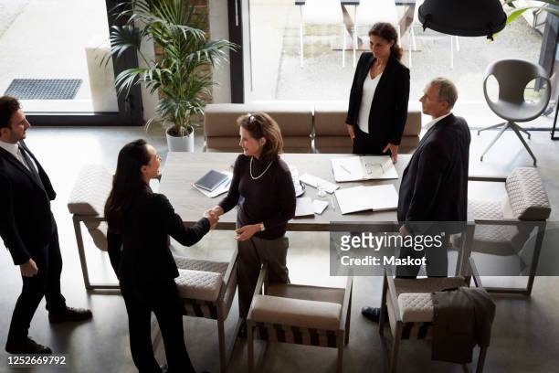high angle view of female financial advisor greeting businesswoman while colleagues standing in office during meeting - regulation stock-fotos und bilder