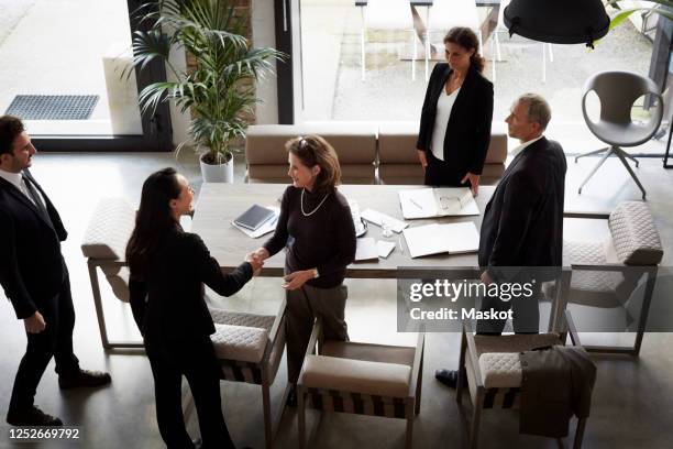 high angle view of female financial advisor greeting businesswoman while colleagues standing in office during meeting - investor conference stock pictures, royalty-free photos & images