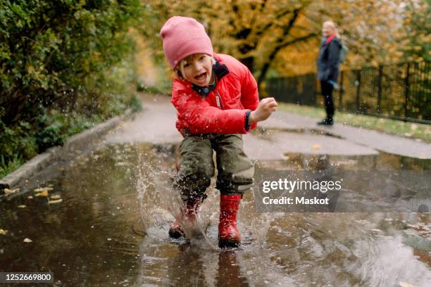 playful boy splashing water in puddle on road - family shoes stock-fotos und bilder