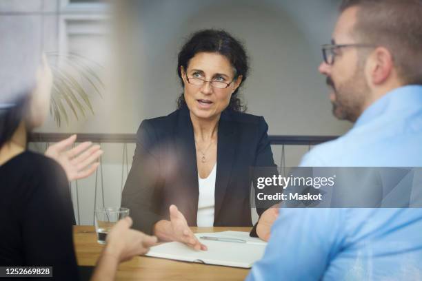 confident mature female lawyer discussing with businessman and businesswoman during meeting at office - advocaat juridisch beroep stockfoto's en -beelden