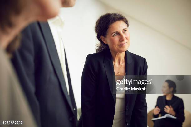 confident businesswoman looking away while standing with lawyers at office during meeting - mid aged stock pictures, royalty-free photos & images