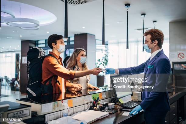 one young couple and male receptionist with protective face masks at the hotel reception - serbia covid stock pictures, royalty-free photos & images