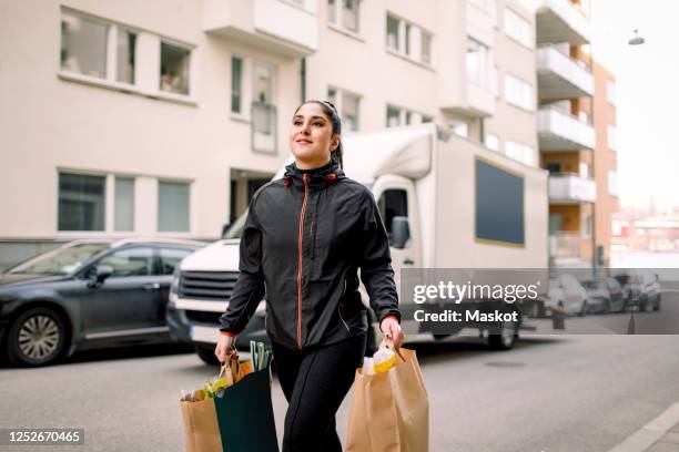 young delivery woman carrying grocery bags while walking on street in city - brown paper bag stock pictures, royalty-free photos & images