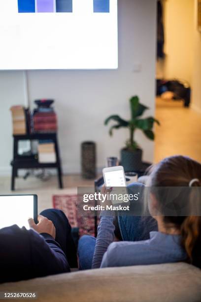 father and daughter using portable devices while sitting on sofa at home - smart tv stock pictures, royalty-free photos & images