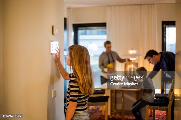 girl using digital tablet on wall with family in background at smart home - home technology stock-fotos und bilder