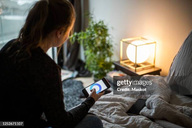 teenage girl using smart phone app while adjusting lighting equipment in bedroom at smart home - copilot ストックフォトと画像