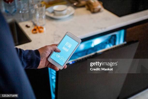cropped image of man using mobile app against dishwasher at smart home - major household appliance stock pictures, royalty-free photos & images