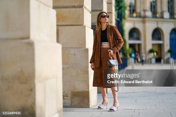 Natalia Verza wears Celine sunglasses, a necklace, a black Paco Rabanne cropped top, a Gestuz brown suede jacket, brown suede long shorts, white...