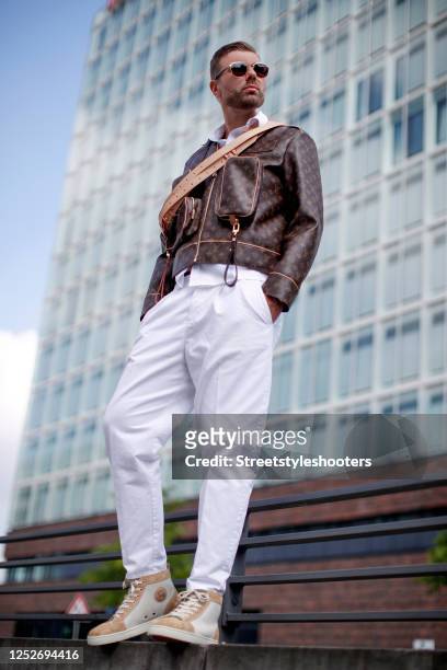 Influencer Andre Borchers wearing a brown monogram admiral jacket by Louis Vuitton, beige and caramel colored sneaker by Christian Louboutin, white...