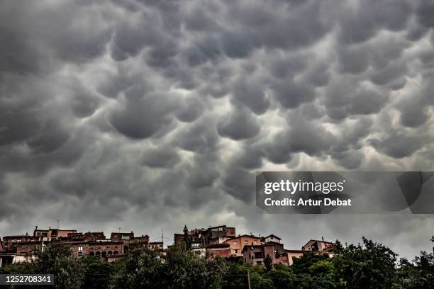 dramatic stormy sky with mammatus cloud and rural town in the pyrenees. - mammatus cloud stock pictures, royalty-free photos & images