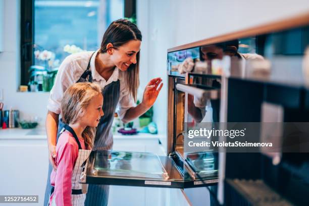 moeder en dochter die oven openen om voedsel te controleren. - hot wife stockfoto's en -beelden