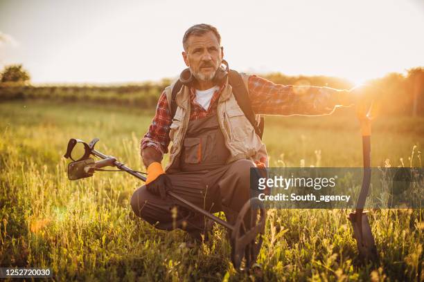 senior man looking for treasures in nature with the metal detector - treasure hunt stock pictures, royalty-free photos & images
